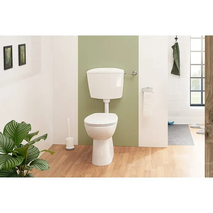 Calmwaters Stand-WC-Set Spülrandlos mit Erhöhung - Spülrandlos, Ohne Spezialglasur, Spülform: Tief, WC Abgang: Waagerecht, Weiß - Eine Nahaufnahme einer weißen Toilette mit Spülkasten in einem Badezimmer mit Holzboden, umgeben von Pflanzen und Handtüchern.