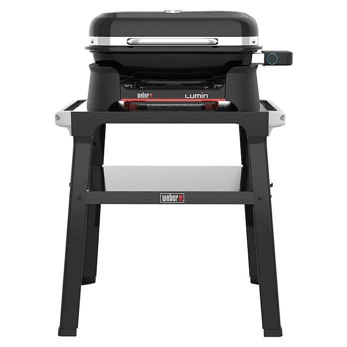 Weber Elektrogrill Lumin mit Grilltisch - Grillfläche (B x T): 49 x 33 cm, 2,2 kW - Ein Weber Lumin Elektrogrill mit Ständer, perfekt für den Balkon. Der Grill ist schwarz mit silbernen Akzenten und einem roten "Lumin"-Schriftzug.