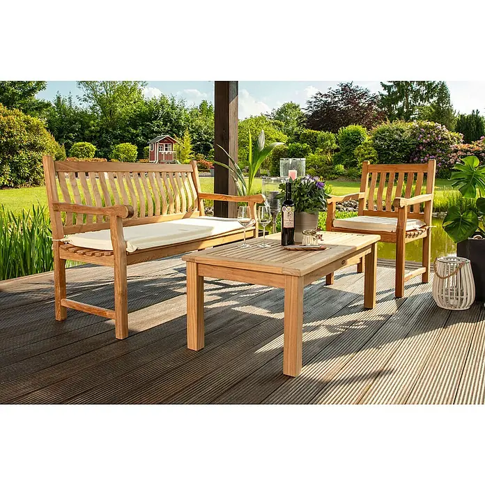 Kai Wiechmann Garten-Beistelltisch - Teakholz, Rechteckig, Naturbelassen - Teakholz-Gartenmöbelset mit Bank, Stuhl und Tisch auf einer Terrasse mit üppigem Grün im Hintergrund.