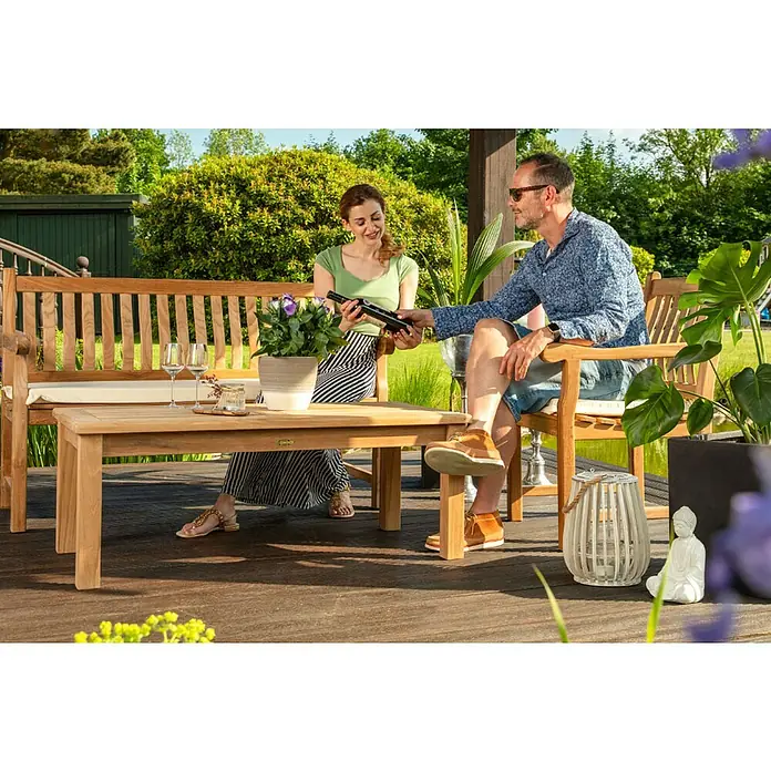 Kai Wiechmann Garten-Beistelltisch - Teakholz, Rechteckig, Naturbelassen - Entspanntes Paar genießt einen Moment auf einer Holzbank im Garten, mit Tisch, Weingläsern und stilvoller Dekoration.