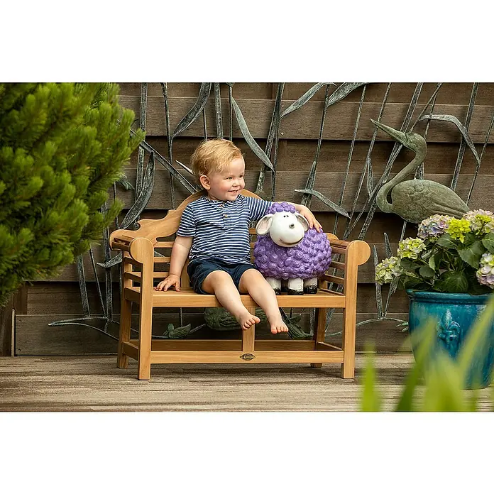 Kai Wiechmann Kinder-Gartenstuhl - Teakholz, Naturbelassen, B x T x H: 80 x 33 x 60 cm - Entzückender Junge sitzt mit einem lila Schaf auf einer Holzbank im Garten, umgeben von üppigem Grün und dekorativen Gartenelementen.
