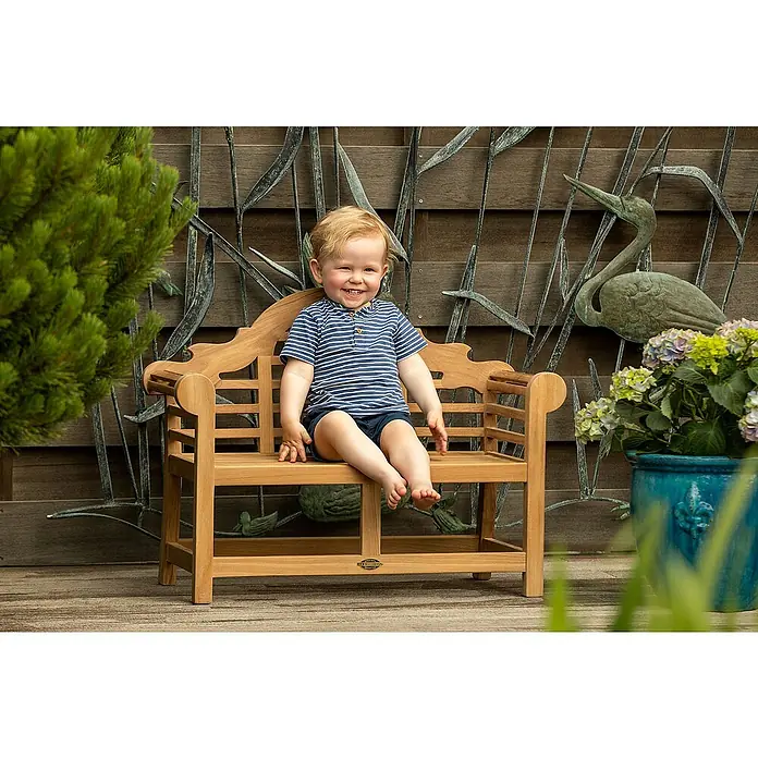 Kai Wiechmann Kinder-Gartenstuhl - Teakholz, Naturbelassen, B x T x H: 80 x 33 x 60 cm - Lächelnder Junge sitzt auf einer kleinen Gartenbank aus Holz vor dekorativer Wand.