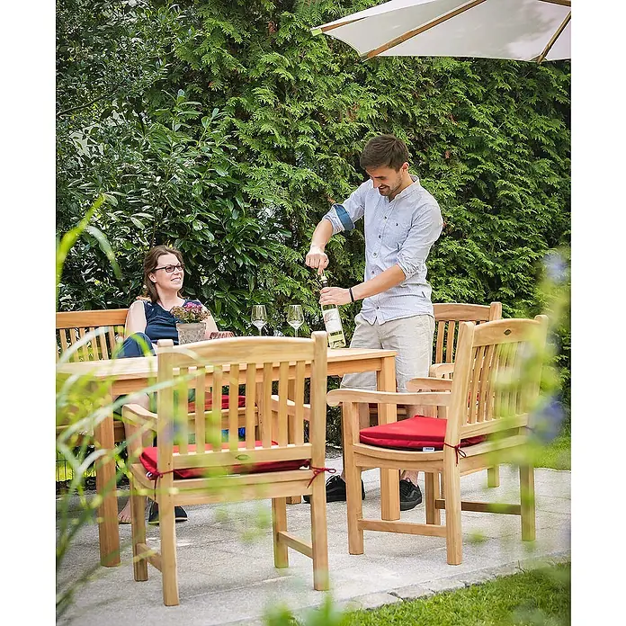 Kai Wiechmann Sitzauflage - Sessel, L x B x H: 45 x 50 x 5 cm, Polyacryl, Bordeauxrot - Ein Mann öffnet eine Flasche Wein an einem Gartentisch mit Stühlen und einer Frau, die das entspannte Ambiente genießt.