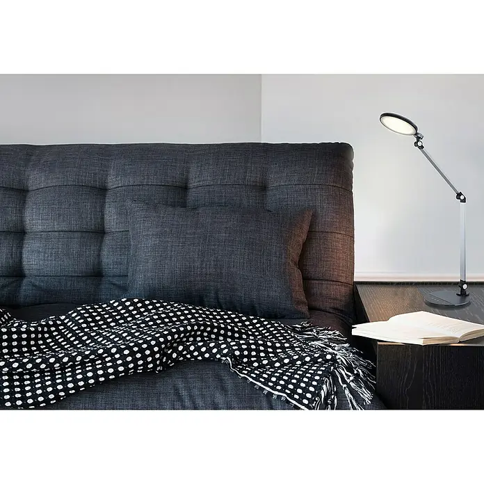 Globo Tischleuchte Konsti - 9 W, L x B x H: 50 x 19,2 x 90,5 cm, Grau/Schwarz - Nahaufnahme einer modernen, silberfarbenen LED-Schreibtischlampe neben einem Buch auf einem Nachttisch, perfekt für gemütliche Lesestunden.
