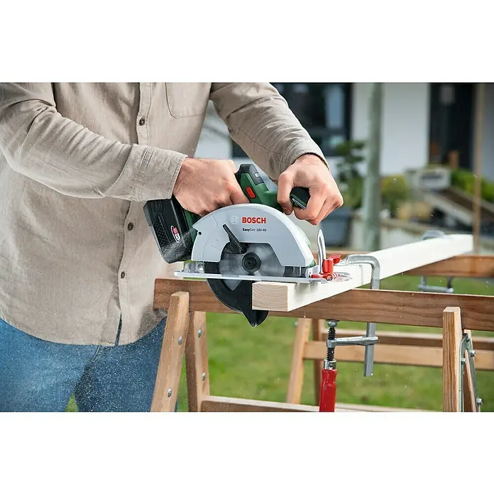 Bosch Power for All 18V Akku-Handkreissäge EasyCirc 18V-48 - 18 V, Ohne Akku, Durchmesser Sägeblatt: 150 mm, 4.200 U/min - Ein Mann sägt mit einer Bosch EasyCirc 18V-48 Kreissäge ein Holzbrett. Die Säge ist kabellos und hat einen Akku.