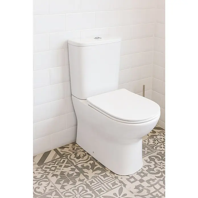 Camargue Pack de WC Malta - Sin borde de descarga, Salida WC: Horizontal, Blanco - Elegante inodoro en blanco sobre una pared de azulejos blancos y un suelo estampado. El inodoro es moderno y encaja bien en el baño.