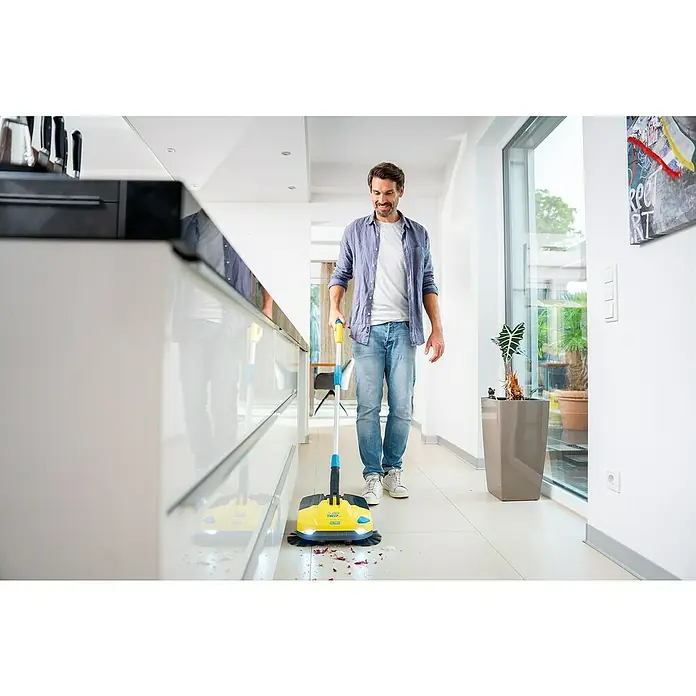 Gloria Power for All 18V Akku-Handkehrmaschine EasySweep 18V - 18 V, 1 Akku, Arbeitsbreite: 40 cm, 4,5 l - Ein Mann benutzt einen gelben Akku-Besen zur Reinigung des Küchenbodens. Praktisches Gerät für schnelles und einfaches Aufsammeln von Schmutz und Krümeln.