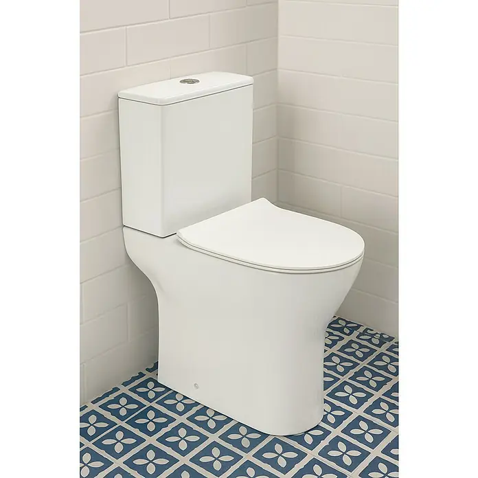 Pack de WC Setúbal - Sin borde de descarga, Salida dual, Blanco - Primer plano de un inodoro blanco moderno con cisterna cuadrada y tapa de asiento a juego sobre una pared de ladrillo blanco y un suelo estampado.