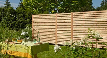 Holzzaun als Sichtschutz im Garten, davor ein Tisch mit Getränke