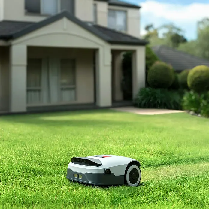 Anthbot Mähroboter Genie 3000 - 3.600 m², Schnittbreite: 20 cm, Satellitengestützte Navigation, RTK - Ein moderner Rasenmähroboter steht auf einem grünen Rasen vor einem Wohnhaus, der für eine automatische Rasenpflege sorgt.