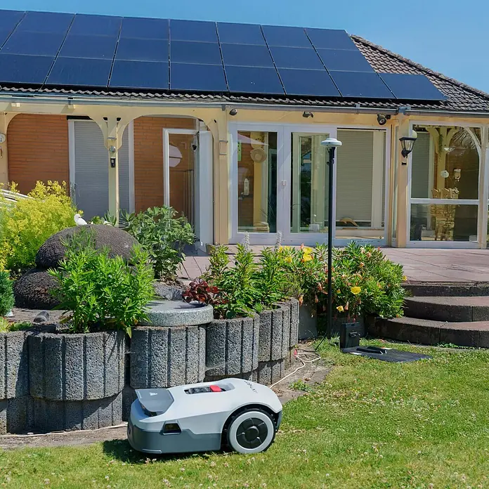 Anthbot Mähroboter Genie 3000 - 3.600 m², Schnittbreite: 20 cm, Satellitengestützte Navigation, RTK - Rasenmähroboter vor einem Haus mit Solaranlage, der den Rasen automatisch pflegt. Erleichtert die Gartenarbeit und spart Zeit.