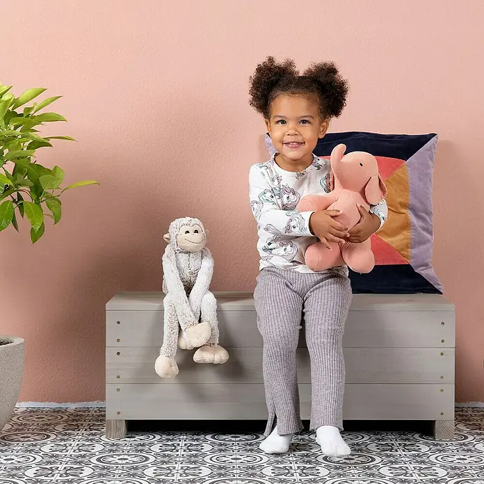 Muddy Buddy Bank Discoverer - 83 x 35 x 32 cm, Holz, Warmgrau - Lachendes Mädchen umarmt rosa Elefantenkuscheltier, während ein Plüschaffe daneben sitzt. Niedliches Kinderzimmerdekor.
