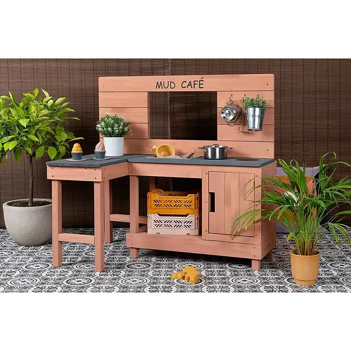 Muddy Buddy Matschküche Coffee Corner - 100 x 60 x 95 cm, Holz, Puderrosa - Foto eines Outdoor-Spielküche „Mud Café“ aus Holz mit Spielzeug auf einem gemusterten Boden vor braunem Hintergrund.