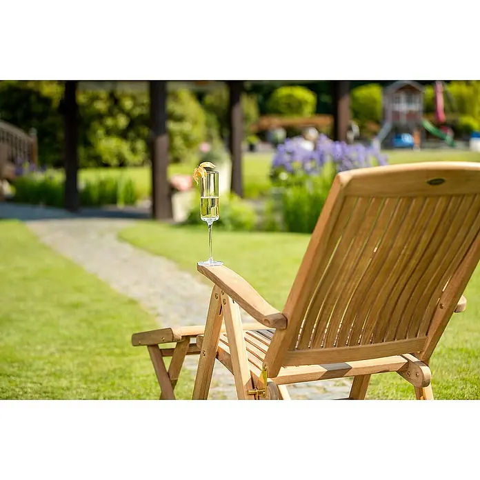 Kai Wiechmann Gartenstuhl - Teakholz, Klappbar, Naturbelassen, B x T x H: 63 x 77 x 110 cm - Ein Champagnerglas mit Garnierung steht auf einem hölzernen Liegestuhl im Garten, der zum Entspannen im Freien einlädt.