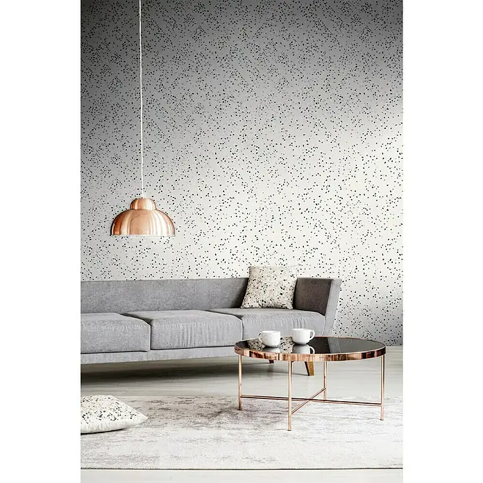 A.S. Création New Walls Vliestapete Grafik - Weiß/Schwarz, Grafisch, 10,05 x 0,53 m - Wohnzimmer mit grauem Sofa, Kupferlampe und Couchtisch mit zwei Tassen. Die Wand hat ein gesprenkeltes Muster.