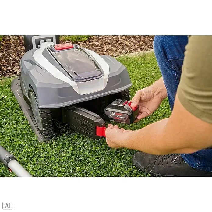 AL-KO 18V/36V Mähroboter Robolinho 500 Vision - 500 m², Schnittbreite: 20 cm, Kamera-gestützte Navigation - Ein Mann setzt einen 18V Akku in einen grauen Rasenmähroboter ein. Der Akku ist rot und schwarz, und der Rasenmäher steht auf grünem Gras.
