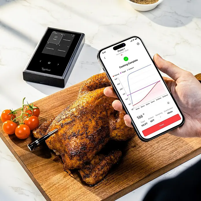 Typhur Grill-Thermometer Sync Quad - 5 -tlg., Kabellos; Verbindung via Bluetooth oder Wi-Fi - Aufnahme eines Typhur-Thermometers neben einem gebratenen Hähnchen und einem Smartphone, das die Garparameter anzeigt.