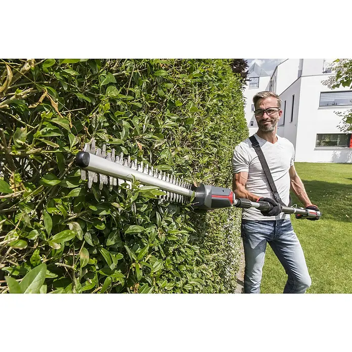 AL-KO 18V/36V Akku-Heckenschere HTAD 1845 - 18 V, Li-Ionen, 1 Akku, Schnittlänge: 45 cm - Ein Mann benutzt eine Heckenschere, um eine grüne Hecke zu schneiden. Die Heckenschere ist mit einem Schultergurt versehen.