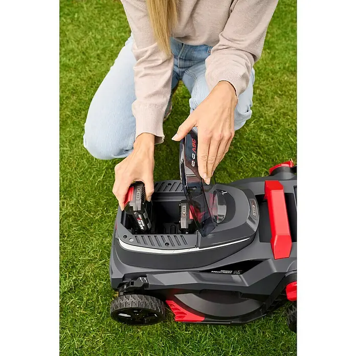 AL-KO 18V/36V Akku-Rasenmäher 34.6 - 18 V - 36 V, 2 Akkus, 2,5 Ah, Schnittbreite: 34 cm - Eine Frau setzt einen Akku in einen grauen Rasenmäher mit roten Akzenten.