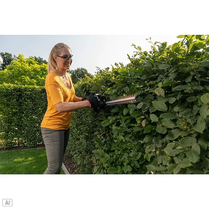 AL-KO 18V/36V Akku-Heckenschere HTD 1855 - Li-Ionen, Ohne Akku, Schnittlänge: 55 cm - Eine Frau schneidet mit einer Akku-Heckenschere eine grüne Hecke im Garten, wobei sie Schutzbrille und Handschuhe trägt.