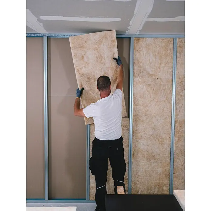 Isover Lanaé Glaswolle Trennwandplatte WLS 040 - Stärke: 50 mm, Wärmeleitfähigkeit: 0,04 W/(mK) - Ein Bauarbeiter installiert Dämmplatten an einer Wand, die mit Metallrahmen verstärkt ist, um die Wärmeisolierung zu verbessern.