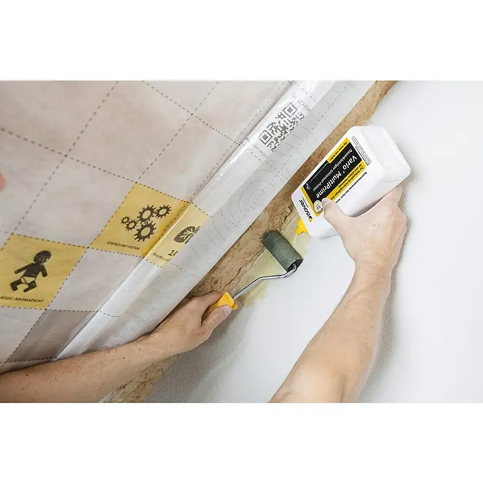 Isover Vario Primer Multiprime - 1 l - Eine Person trägt Isover Vario MultiPrime Kleber mit einem Roller auf eine Oberfläche auf, um eine dauerhafte Verbindung zu gewährleisten.