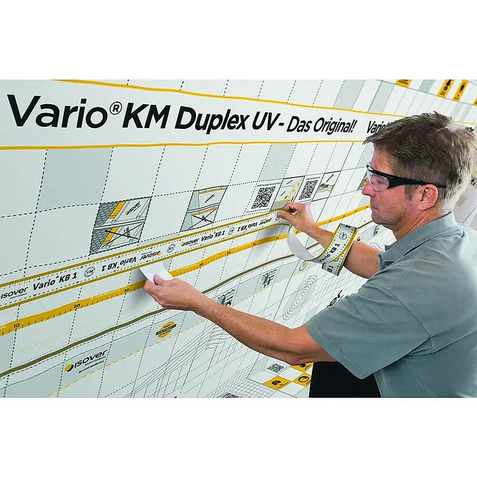 Isover Vario Klebeband KB1 - L x B: 40 m x 60 mm - Ein Mann befestigt Isover Vario KB 1 Dichtband an einer Wand, um die Luftdichtheit zu gewährleisten.