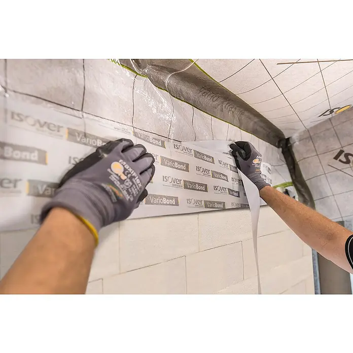 Isover Vario Putzband Bond 150 - L x B: 25 m x 150 mm - Anbringen von Isover VarioBond Dichtband für eine luftdichte Gebäudehülle, demonstriert durch Handwerker mit Arbeitshandschuhen.