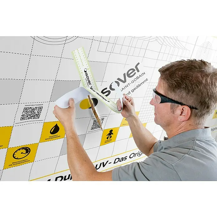 Isover Vario Klebeband MultiTape + - 25 m x 60 mm - Ein Mann befestigt das Isover Vario MultiTape+ auf einer Wand mit Produktinformationen, um eine optimale Abdichtung zu gewährleisten.