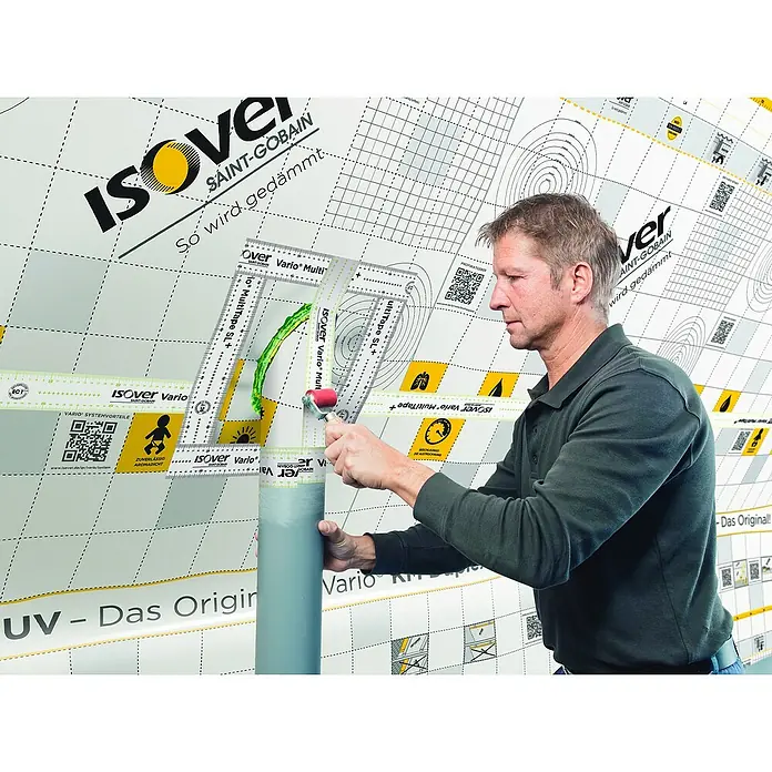 Isover Vario Klebeband MultiTape + - 25 m x 60 mm - Anwendung von Isover Vario MultiTape+: Der Handwerker dichtet ein Rohr mit dem Dichtband auf einer Isover-bedruckten Folie ab.