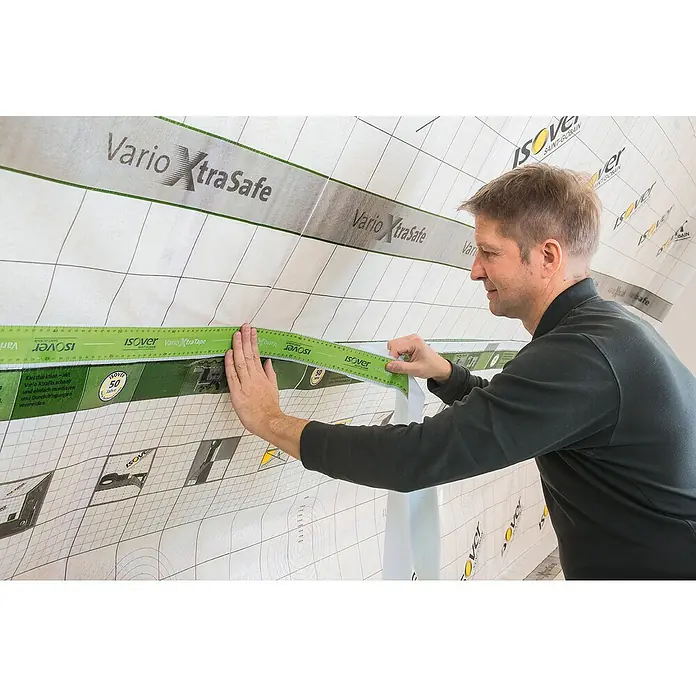 Isover Vario Klebeband XtraTape - 20 m x 60 mm - Ein Mann bringt eine Isover Vario XtraSafe Folie an, ein feuchtevariables Klimamembran, das hilft, Bauschäden zu vermeiden und die Energieeffizienz zu verbessern.