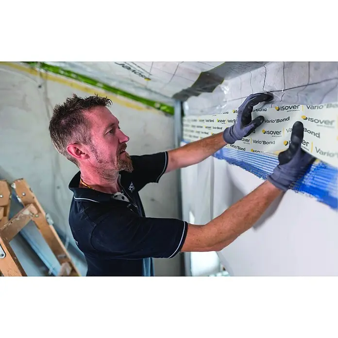 Isover Vario Putzband Bond 150 - L x B: 25 m x 150 mm - Ein Mann montiert Isover Vario Bond Dampfbremsfolie, um die Gebäudeisolierung zu verbessern und Feuchtigkeitsschäden zu verhindern.