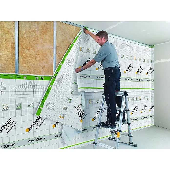 Isover Dampfbremsfolie XtraSafe - L x B: 40 x 1,5 m, 60 m² - Ein Mann montiert Isover Vario XtraSafe Dampfbremsfolie an einer Wand auf einer Leiter, um die Wärmedämmung zu verbessern.