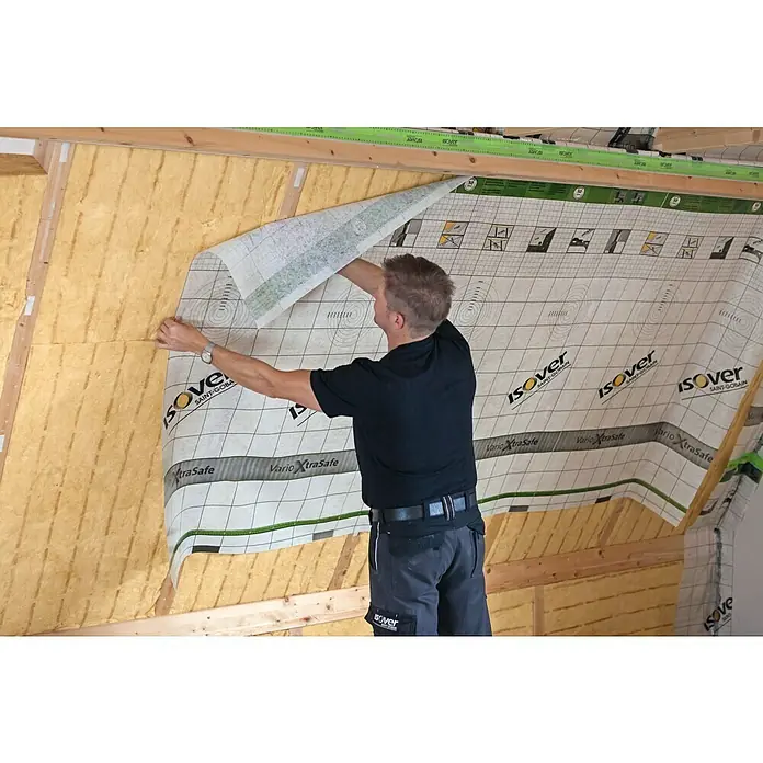 Isover Dampfbremsfolie XtraSafe - L x B: 40 x 1,5 m, 60 m² - Ein Mann befestigt eine Isover Vario XtraSafe Dampfbremsfolie an einer Wand mit Glaswollisolierung, um Feuchtigkeit zu regulieren.