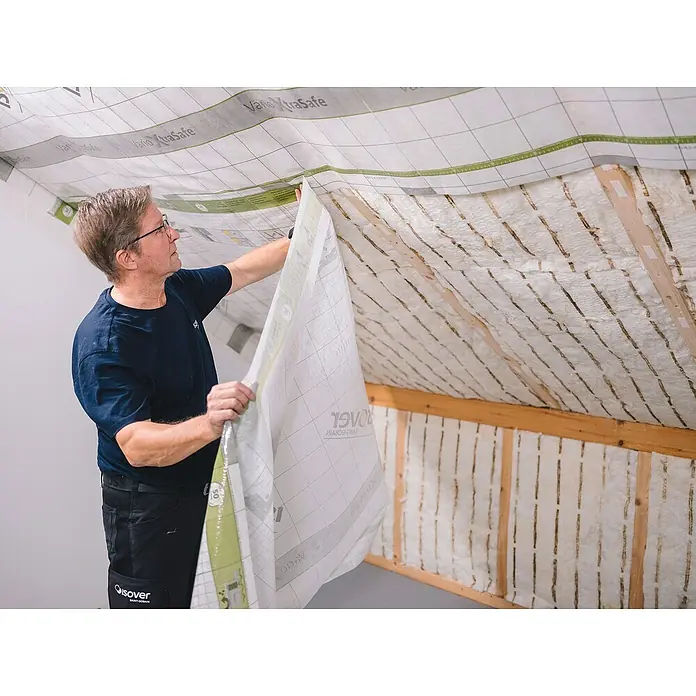 Isover Dampfbremsfolie XtraSafe - L x B: 40 x 1,5 m, 60 m² - Ein Mann befestigt eine Vario XtraSafe Dampfbremsfolie an einer Dachschräge mit Dämmwolle zwischen den Dachsparren.