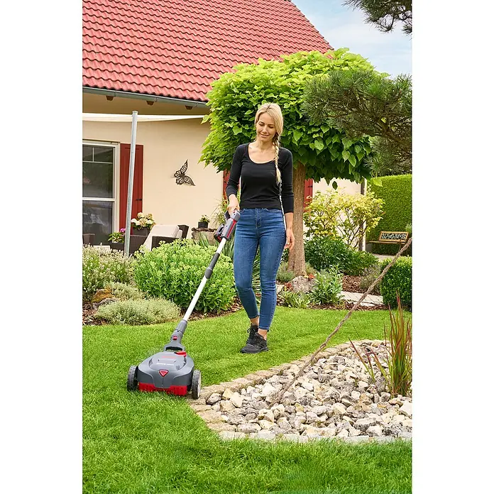 AL-KO 18V/36V Akku-Rasenmäher 22.6 - 18 V, Ohne Akku, Schnittbreite: 22 cm - Frau arbeitet mit einem Akku-Rasentrimmer im Garten. Das Gerät ist rot/grau und verfügt über einen Teleskopstiel für mehr Komfort.