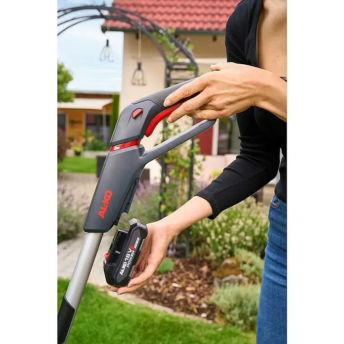 AL-KO 18V/36V Akku-Rasenmäher 22.6 - 18 V, Ohne Akku, Schnittbreite: 22 cm - Eine Frau setzt einen AL-KO 18V Akku in einen AL-KO Rasentrimmer ein. Praktisches Gartengerät für präzise Rasenpflege ohne Kabel.