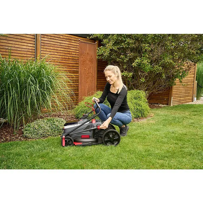 AL-KO 18V/36V Akku-Rasenmäher 38.6 - 18 V - 36 V, 2 Akkus, 4 Ah, Schnittbreite: 38 cm - Frau justiert einen Rasenmäher im Garten. Der Rasenmäher ist schwarz mit roten Akzenten.