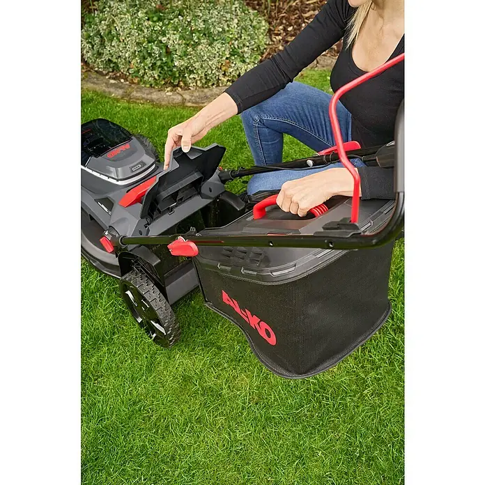AL-KO 18V/36V Akku-Rasenmäher 38.6 - 18 V - 36 V, 2 Akkus, 4 Ah, Schnittbreite: 38 cm - Eine Frau bereitet einen AL-KO Rasenmäher mit Fangkorb auf einem grünen Rasen für die Gartenarbeit vor.