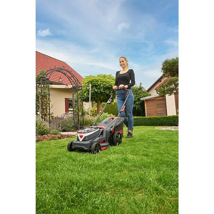 AL-KO 18V/36V Akku-Rasenmäher 38.6 - 18 V - 36 V, 2 Akkus, 4 Ah, Schnittbreite: 38 cm - Frau, die mit einem AL-KO Akku-Rasenmäher im Garten den Rasen mäht, vor einem Haus mit Gartenbogen und Büschen.