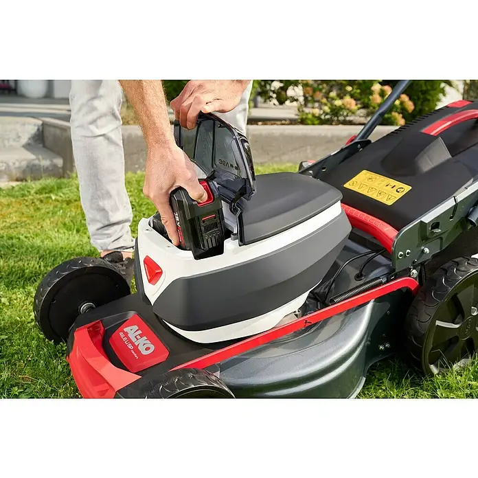 AL-KO 18V/36V Akku-Rasenmäher 46.6 - 18 V - 36 V, 2 Akkus, 5 Ah, Schnittbreite: 46 cm - Ein Mann setzt einen Akku in einen AL-KO Rasenmäher ein. Der Rasenmäher ist rot, schwarz und weiß.