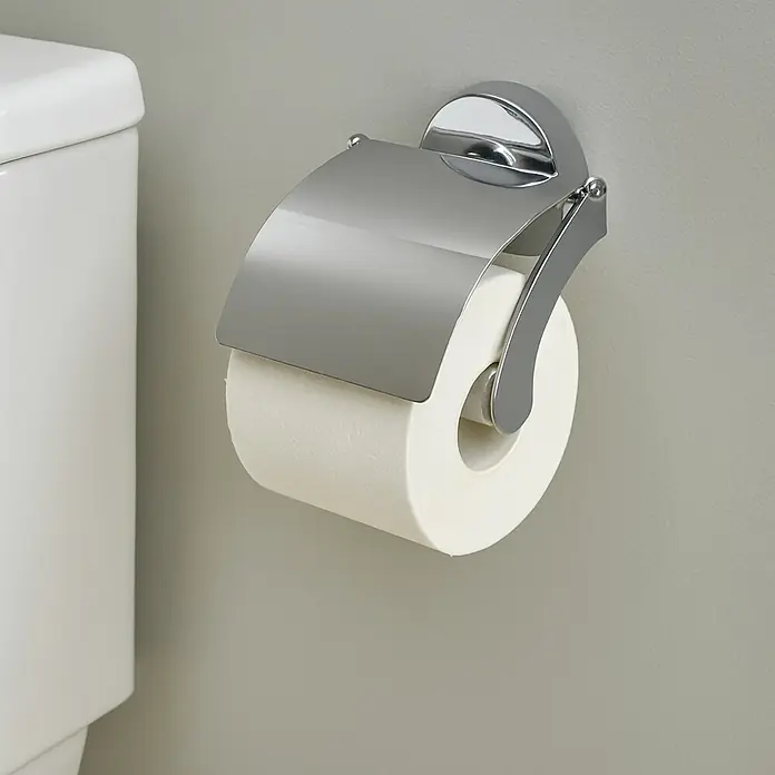 Venus Marina Portarrollos papel higiénico - Con tapa, Crromo, Resplandeciente - Dispensador de papel higiénico con cubierta cromada y rollo de papel higiénico en una pared gris junto a un inodoro blanco.