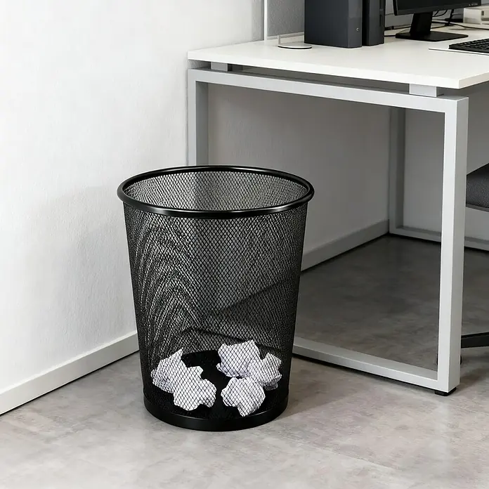 Papierkorb - Metall, Schwarz - Nahaufnahme eines schwarzen Papierkorbs mit zerknülltem Papier, der unter einem Schreibtisch in einem Büro steht.