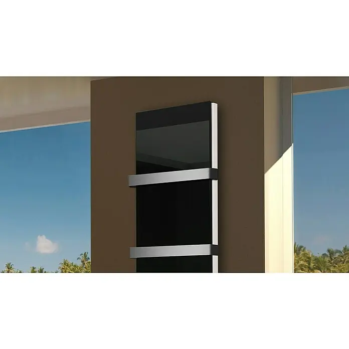 Badheizkörper Montevideo - B x H: 470 x 1.800 mm, Nennleistung: 1.964 W, Schwarz, 2 x Halter 50mm - Moderner Handtuchwärmer in Schwarz mit silbernen Halterungen an einer braunen Wand, vor einem Fenster mit Blick auf einen blauen Himmel und Palmen.