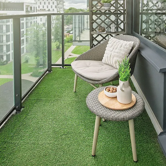 ML-Design Kunstrasen Bodenbelag mit Klicksystem und Drainage - 30 x 30 cm, Grün - Einladender Balkonbereich mit Kunstrasen, einem Rattansessel mit Kissen und einem Beistelltisch mit Deko für entspannte Stunden im Freien.