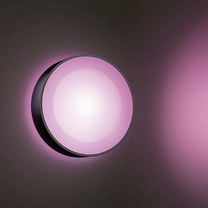 Philips Hue LED-Außenwandleuchte White & Color Ambiance Daylo - 15 W, 22 x 22 x 7,6 cm, Schwarz, IP44 - Diese Aufnahme zeigt eine moderne runde Wandleuchte mit einem rosa Schein und einem dunklen Rahmen, die eine stilvolle Atmosphäre erzeugt.