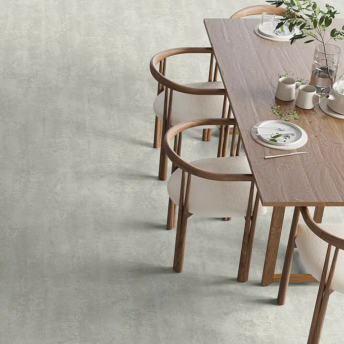 b!design Vinylboden SPC - Hellas, Fliese, 609,6 x 304,8 x 3,8 mm - Ein heller Esstisch aus Holz mit Geschirr und Dekoration steht auf einem modernen Bodenbelag, umgeben von Stühlen mit hellem Bezug.
