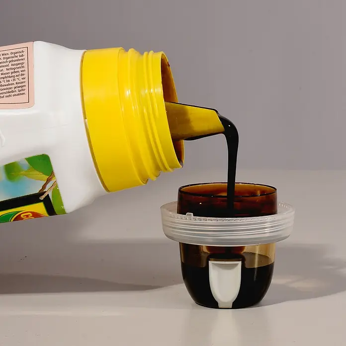 Compo Zitrusdünger - 0,5 l - Eine Flasche mit gelbem Hals gießt dunkle Flüssigkeit in einen Messbecher.