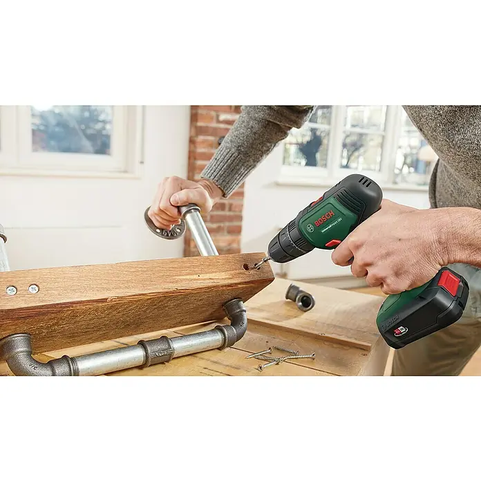 Bosch Power for All 18V Akkuschrauber UniversalImpact 18V - 18 V, 2 Akkus, 1,5 Ah, 241 -tlg. - Nahaufnahme eines Bosch UniversalImpact 18V Akku-Bohrschraubers beim Arbeiten an einem Holzprojekt mit Metallrohren.