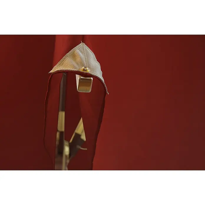 Kai Wiechmann Marktschirm - Rot|Bordeaux|Bordeauxrot|Weinrot - Nahaufnahme einer mittelalterlichen Stoffhaube, befestigt an einer Halterung vor einem roten Hintergrund.